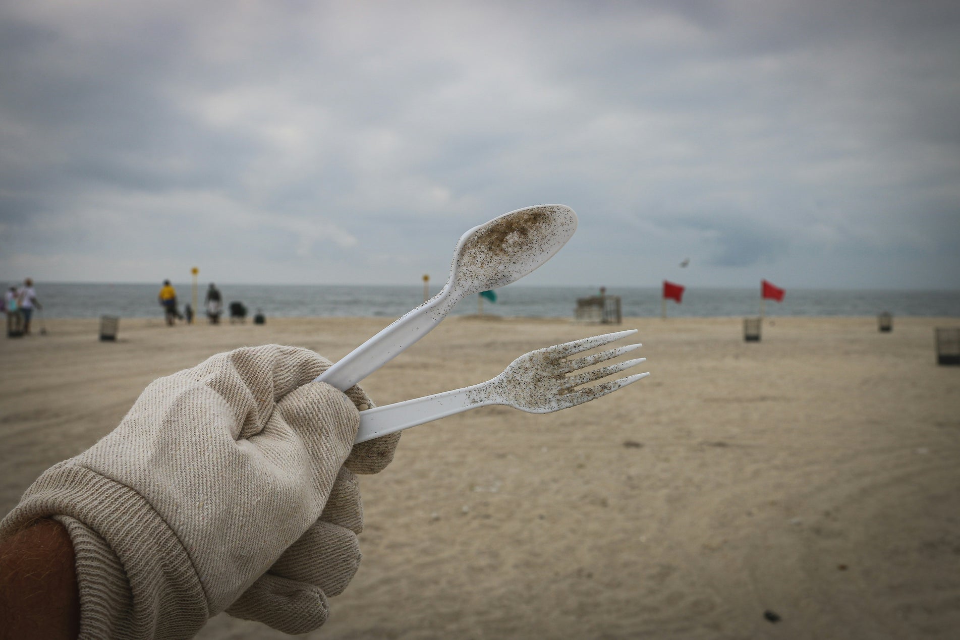 Hand hält verschmutztes Plastikbesteck als Symbol für die Verschmutzung der Meere.