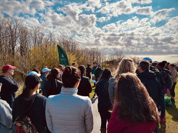 Eine Gruppe von Menschen versammelt sich bei einer Aufforstungsaktion. Ein Mitarbeiter der Firma Becher spricht zu den Teilnehmern unter einem bewölkten Himmel.