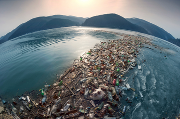 Eine große Menge an Plastikflaschen und anderem Müll schwimmt auf der Oberfläche eines Sees, umgeben von Bergen. Dies veranschaulicht die schwerwiegenden Umweltprobleme durch Plastikverschmutzung in Gewässern.